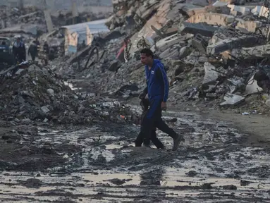 Warga Palestina berjalan di tengah bangunan yang hancur akibat serangan udara dan darat Israel di Kota Gaza, Selasa 6 Januari 2026. Komite Internasional Palang Merah (ICRC) terus berupaya menyalurkan bantuan ke Gaza. (AP Photo/Jehad Alshrafi)