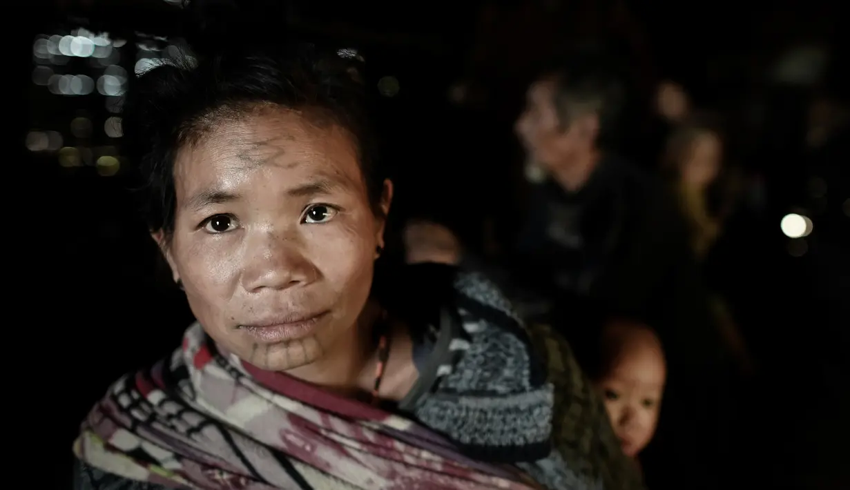 Ku Myo (35), seorang wanita suku Lainong yang bertato menggendong anaknya di rumah mereka di Kota Lahel, Sagaing, Myanmar, 8 Februari 2020. Suku-suku tersebut menjalin kepercayaan animisme mereka dengan tradisi prajurit yang mencakup desain tato mencolok. (Ye Aung THU/AFP)