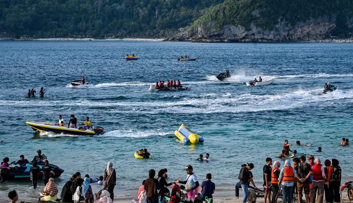 Dikenal sebagai salah satu titik selancar terbaik di Indonesia, Lhoknga memiliki ombak yang menantang dengan ketinggian rata-rata 1,5 hingga 2 meter. Tampak dalam foto, orang-orang saat berkumpul menikmati masa libur panjang Idulfitri di area olahraga air, Pantai Lhoknga, Aceh, pada Kamis 26 Maret 2026. (Chaideer MAHYUDDIN/AFP)