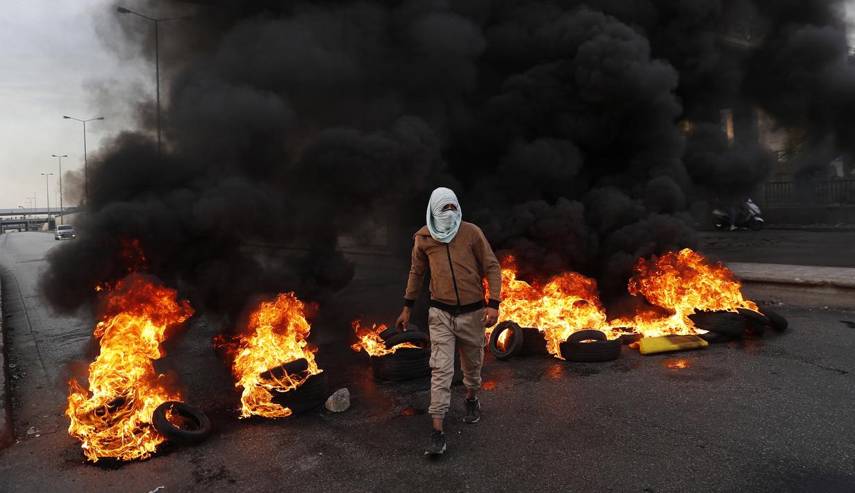 Seorang pengunjuk rasa melewati ban yang terbakar di sepanjang jalan raya utama yang mengarah ke Bandara Internasional Beirut selama protes terhadap kenaikan harga barang-barang konsumen dan jatuhnya mata uang lokal di Beirut, Lebanon, Senin (29/11/2021). (AP Photo/Hussein Malla)