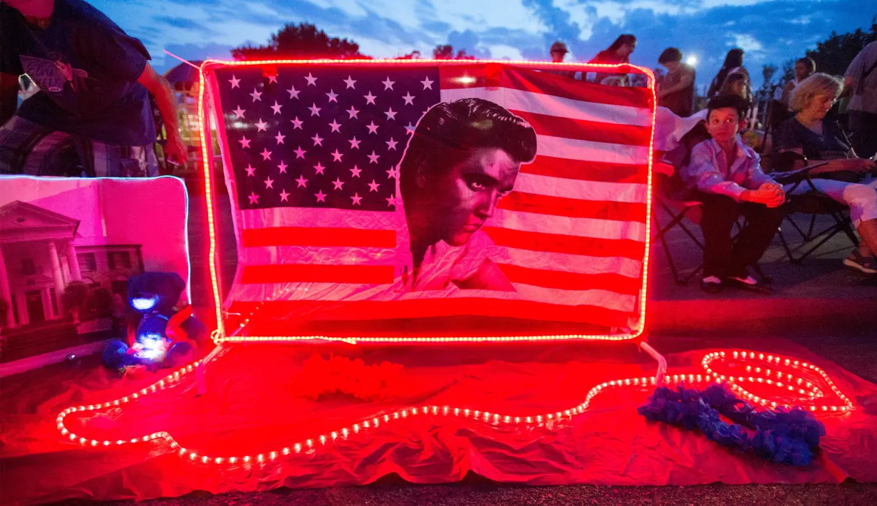 Bendera Amerika dengan wajah Elvis Presley terpajang di depan bekas rumah Elvis di Graceland, Memphis, Tennessee, Selasa (15/8). Para penggemar menghadiri peringatan 40 tahun kematian bintang rock n roll tersebut. (AP Photo/Brandon Dill)