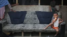 Seorang anak pengungsi Rohingya duduk di sofa yang rusak menikmati es krim di sebuah kamp pengungsi di New Delhi, India (12/9). Pengungsi Rohingya di India diancam pemerintah untuk dideportasi kembali ke Myanmar. (AP Photo/Altaf Qadri)