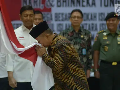 Anak pemimpin Darul Islam/Tentara Islam Indonesia (DI/TII) Sekarmaji Marijan Kartosuwiryo, Sarjono Kartosuwiryo mencium bendera Merah Putih saat pembacaan ikrar setia kepada Pancasila, UUD 45, NKRI dan Bhineka Tunggal Ika di Kemenko Polhukam, Jakarta, Selasa (13/8/2019). (merdeka.com/Imam Buhori)