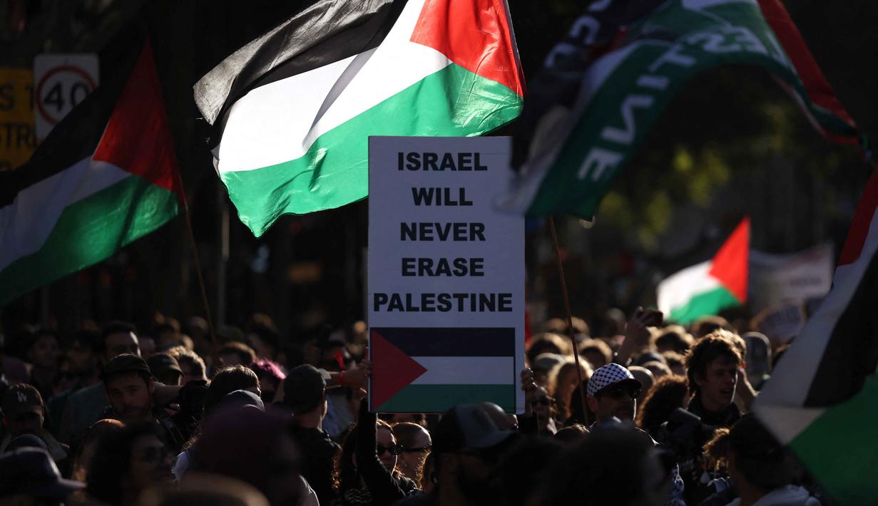Kunjungan Presiden Israel, Isaac Herzog, di Australia dilakukan dengan pengamanan tinggi, aparat keamanan berjaga ketat untuk mengantisipasi potensi gangguan. Tampak dalam foto, para pengunjuk rasa memegang plakat dan bendera saat mereka berunjuk rasa selama kunjungan Presiden Israel, Isaac Herzog, di Melbourne, Australia, pada Kamis 12 Februari 2026. (MARTIN KEEP/AFP)