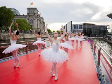 Penari dari Berlin State Ballet menari "Swan Lake" di atas kapal pesiar selama tur pusat kota saat kapal berlayar di depan gedung Reichstag (kiri), Berlin, Jerman, Kamis (10/6/2021). Pertunjukan diikuti oleh banyak orang di sepanjang rute. (Christoph Soeder/dpa via AP)