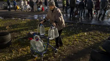 Perempuan lansia mendorong alat bantu jalan yang penuh dengan botol plastik setelah diisi ulang ke dalam tangki, di pusat kota Mykolaiv, Ukraina, Senin (24/10/2022). Sejak pertengahan April warga Mykolaiv telah hidup tanpa pasokan air minum. (AP Photo/Emilio Morenatti)