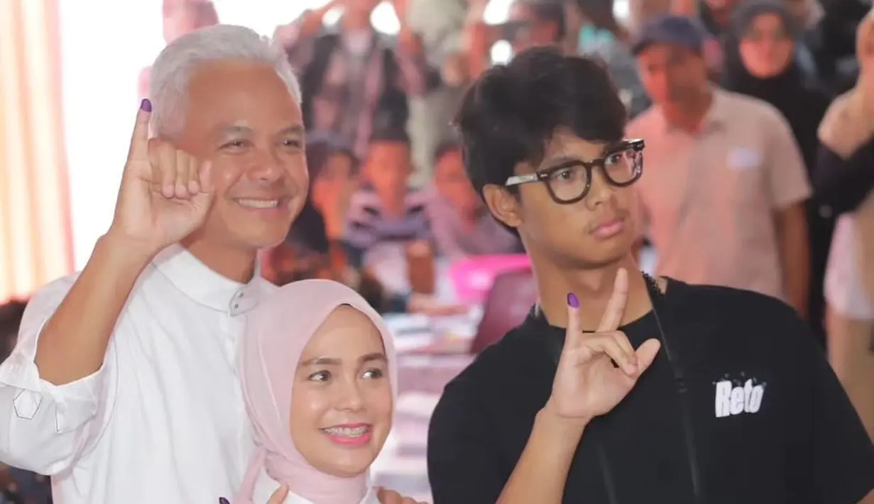 Ia mengenakan kemeja putih yang dipadukan dengan vest warna pink muda. Penampilannya pun dilengkapi dengan hijab segi empat warna pink muda senada dengan vest yang dikenakannya. [@ganjarmahfud.app]