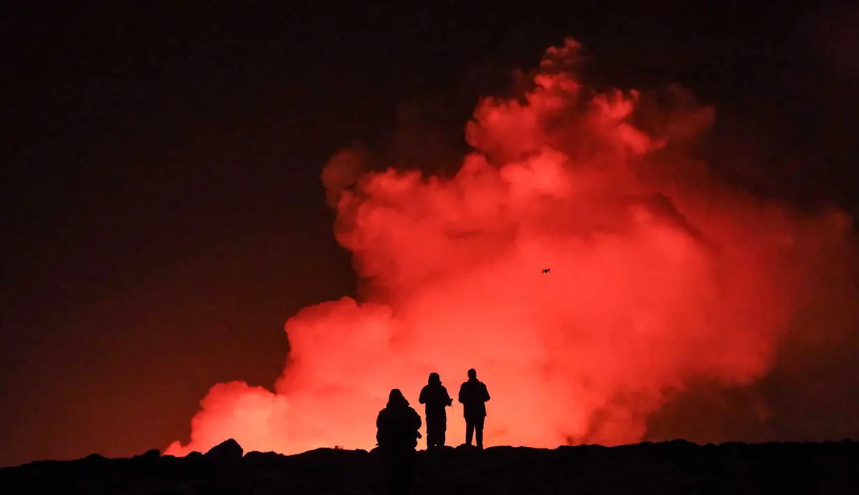 Sekelompok orang mengamati lelehan lava dan asap yang mengepul keluar dari sebuah celah saat terjadi letusan gunung berapi di dekat Grindavik, Islandia barat pada tanggal 8 Februari 2023. (Kristinn Magnusson/AFP/Islandia out)