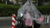 Seorang wanita bermasker menggunakan plastik besar untuk menutupi tubuhnya saat hujan di Beijing (24/5/2022). Beijing memperpanjang perintah bagi pekerja dan pelajar untuk tinggal di rumah dan memerintahkan pengujian massal tambahan pada Senin ketika kasus COVID-19 meningkat di ibu kota China. (AP Photo/Ng Han Guan)