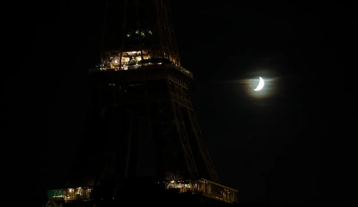 Bulan terlihat di sebelah Menara Eiffel yang lampunya dimatikan di Paris, Rabu (21/10/2020). Kondisi gelap gulita itu untuk memberikan penghormatan terhadap Samuel Paty, seorang guru sejarah yang dipenggal kepalanya pada Jumat (16/10) lalu. (GEOFFROY VAN DER HASSELT / AFP)