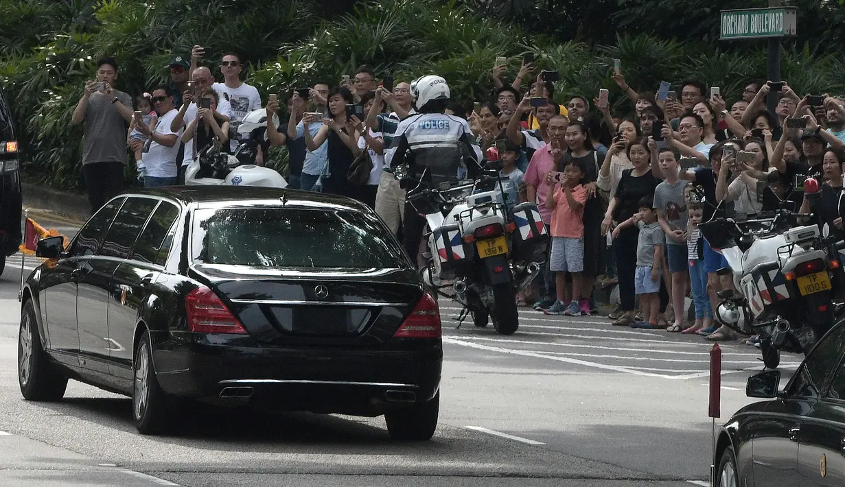 Kerumunan orang menyaksikan iring-iringan mobil yang diyakini membawa pemimpin Korea Utara Kim Jong-un di Orchard Road, Singapura, Minggu (10/6). Puluhan mobil mengawal Kim Jong-un dalam perjalanan menuju hotel St Regis tempatnya menginap (AP/Joseph Nair)