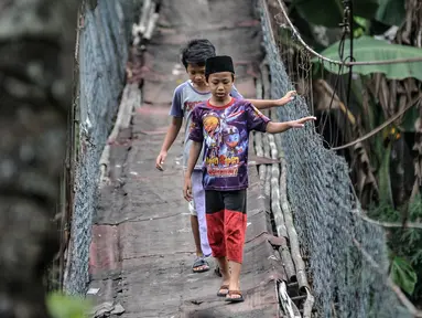 Anak-anak melintasi jembatan gantung yang sudah tidak layak di kawasan Srengseng Sawah, Jakarta, Sabtu (12/6/2021). Jembatan gantung di atas Sungai Ciliwung tersebut saat ini dalam kondisi tidak layak dan dapat membahayakan keselamatan warga yang melintas. (merdeka.com/Iqbal S. Nugroho)