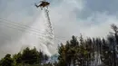 Sebuah helikopter menjatuhkan air ke hutan di atas pepohonan setelah kebakaran hutan di dekat Desa Psachna di pulau Evia (Euboea), pulau terbesar kedua di Yunani, pada 27 Juli 2025. (Angelos TZORTZINIS/AFP)