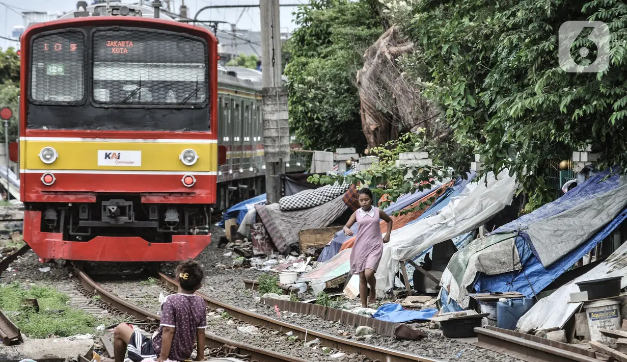 Kereta commuterline melintas di dekat deretan bangunan semipermanen milik tunawisma di kawasan Senen, Jakarta, Minggu (14/2/2021). Sebelumnya pada 2014, pihak KAI membongkar ratusan gubuk tunawisma demi keselamatan perjalanan kereta api serta warga di bantaran rel. (merdeka.com/Iqbal S. Nugroho)