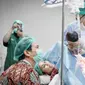 Pada foto lain, seorang dokter memegangi bayi. Dokter berbaju dinas lengkap plus sarung tangan dan penutup kepala memperlihatkan bayi yang baru lahir kepada Gya Sadiqah dan Tarra Budiman. Gya yang mengenakan alat bantu napas tersenyum semringah melibat putri keduanya. Sementara Tarra Budiman yang pakai masker tampak bahagia. Matanya berbinar melihat si kecil. (Foto: Bukaan Moment dari Instagram @gyaps)