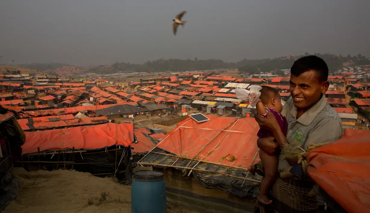 Seorang pria Rohingya menggendong anaknya di tenda pengungsian di kamp pengungsi Jamtoly, Bangladesh (15/1). Media Myanmar melaporkan akan ada 625 bangunan yang mampu menampung sekitar 30.000 orang Rohingya. (AP Photo / Manish Swarup)