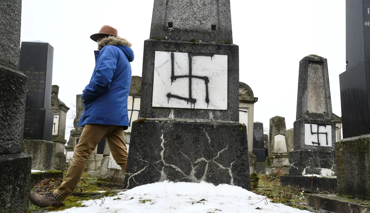 Seorang pria melihat batu nisan yang dicoret-coret lambang swastika nazi di pemakaman Yahudi di Strasbourg, Prancis (17/12). Pihak berwenang belum mengatakan apakah ada hubungan antara aksi vandalisme dengan serangan tersebut. (AFP Photo/Sebastien Bozon)