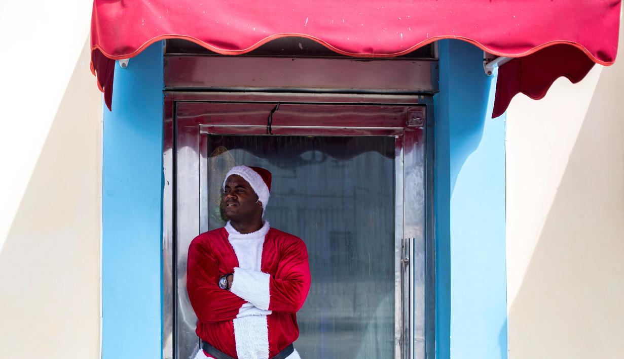 Seorang pria mengenakan pakaian Santa Claus menunggu pelanggan di pintu masuk sebuah kafe di Havana, Kuba (28/12). Havana merupakan kota terbesar dan pelabuhan utama di Kepulauan Hindia Barat. (AP Photo / Desmond Boylan)