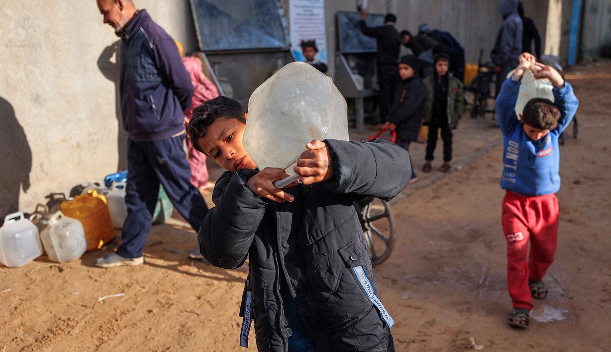 Sebanyak 60% anak usia sekolah saat ini tidak menerima pendidikan tatap muka. Tampak dalam foto, seorang anak laki-laki membawa wadah berisi air dari sumur umum di kamp pengungsi Palestina Nuseirat di utara Deir al-Balah, Jalur Gaza tengah pada 29 Januari 2026. (EYAD BABA/AFP)