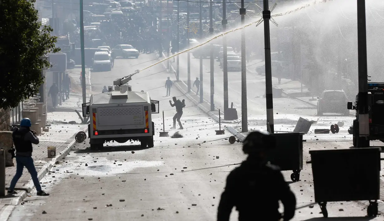 Kendaraan water canon Israel menembakkan air ke arah warga Palestina saat bentrokan di kota Bethlehem, Tepi Barat (7/12). Keputusan Donald Trump mengakui Yerusalem menjadi ibu kota Israel membuat warga Palestina demo. (AP Photo/Nasser Shiyoukhi)