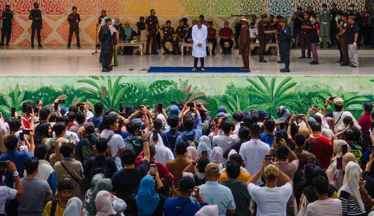 Warga menyaksikan sebelas pria dan wanita menjalani hukuman cambuk setelah dinyatakan bersalah melanggar hukum syariat Islam Aceh yang melarang hubungan seksual di luar nikah di Banda Aceh, Kamis, 20 Agustus 2026. (AFP/ Chaideer Mahyuddin)