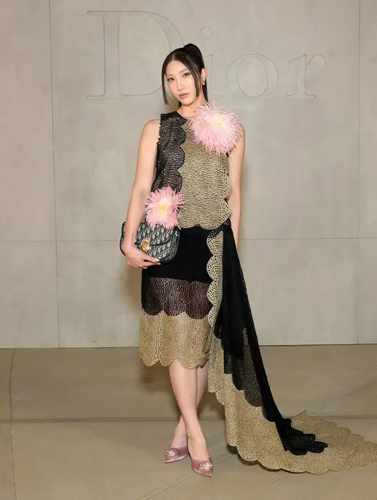 EJAE tampil dengan atasan sleeveless warna gold hitam serasi dengan rok mini dengan aksen menjuntai. Semakin stunning dengan model dua bunga pink besar di bajunya. Sambil membawa tas Dior di tangannya.  [Dok. DIOR]
