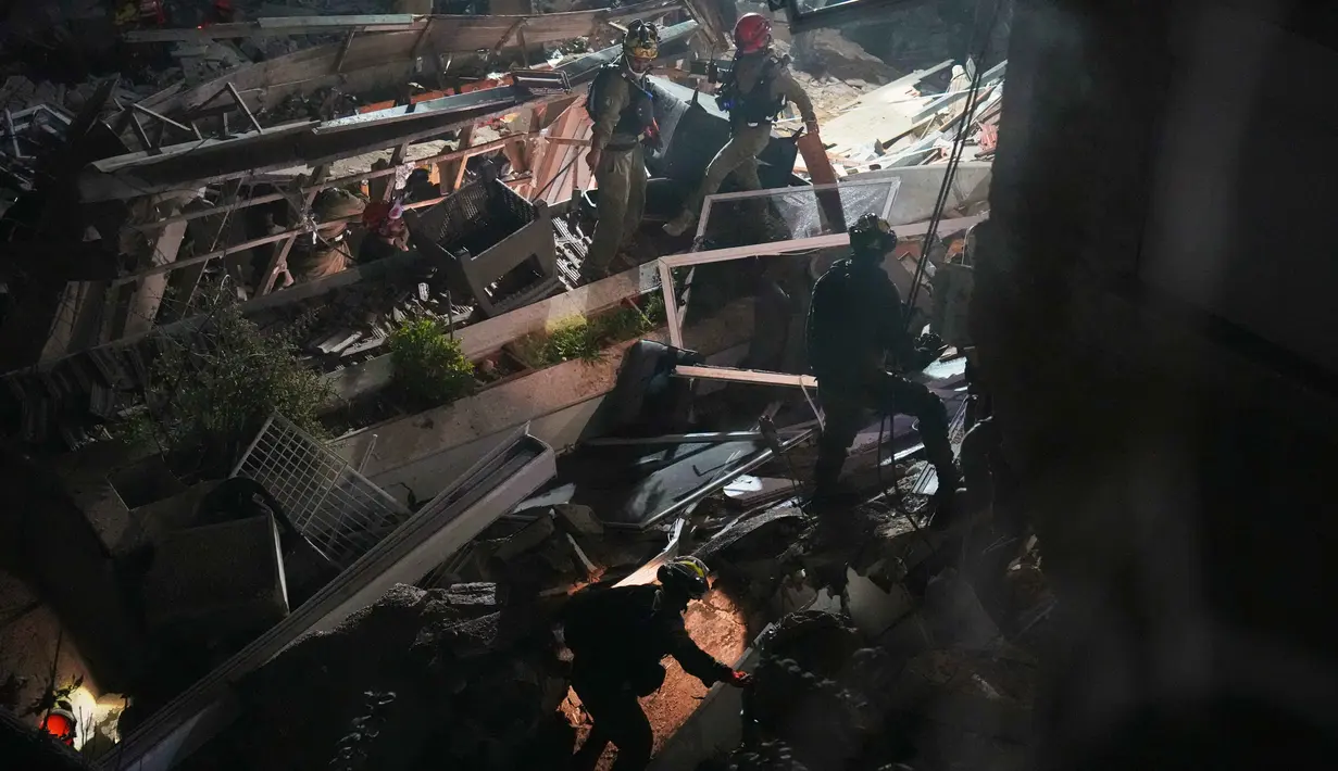 Diduga masih terdapat warga yang terjebak atau hilang di bawah struktur bangunan gedung yang runtuh. Tampak dalam foto, pasukan keamanan Israel dan tim penyelamat melakukan upaya pencarian korban di tengah reruntuhan bangunan tempat tinggal yang dihantam rudal Iran di Haifa, Israel, Minggu, 5 April 2026. (AP Photo/Ariel Schalit)