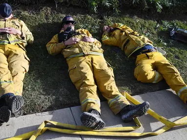 Petugas pemadam kebakaran (damkar) beristirahat setelah kelelahan mengatasi kebakaran yang disebut Lilac Fire di Bonsall, California, Jumat (8/12). Lilac Fire telah menyebar dari 10 hektar menjadi 4.100 hektar hanya dalam beberapa jam. (Robyn Beck/AFP)