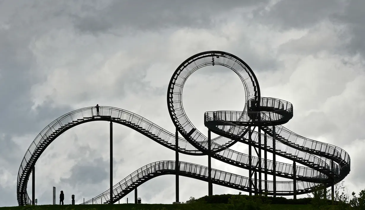 Orang-orang berjalan di sebuah instalasi tangga melingkar "Tiger and Turtle" di Duisburg, Jerman, 30 April 2018. Instalasi seni ini adalah patung jalan setapak menyerupai roller coaster yang berada di atas puncak bukit. (AP/Martin Meissner)