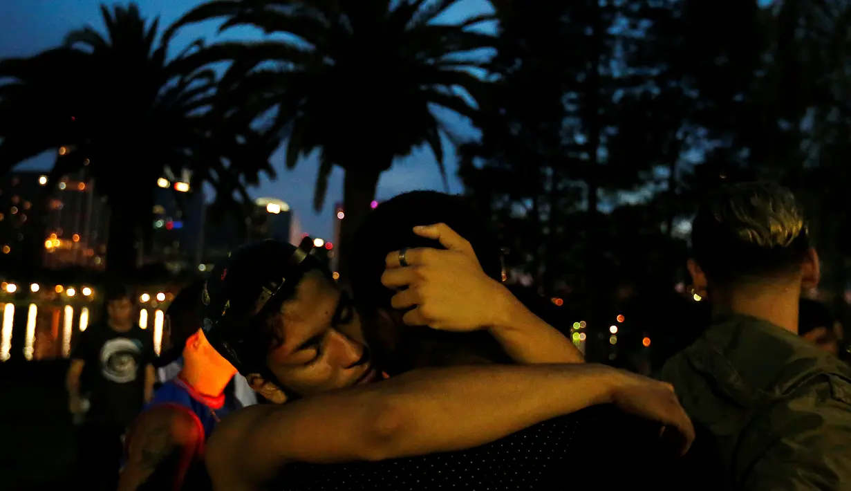 Dua orang pria saling berpelukan di taman setelah teror penembakan di Pulse, klub malam khusus kaum gay di Orlando, Florida, AS, Minggu (12/6). 50 orang tewas dan 53 terluka akibat penembakan yang dilakukan Omar Saddiqui Mateen. (REUTERS/Carlo Allegri)