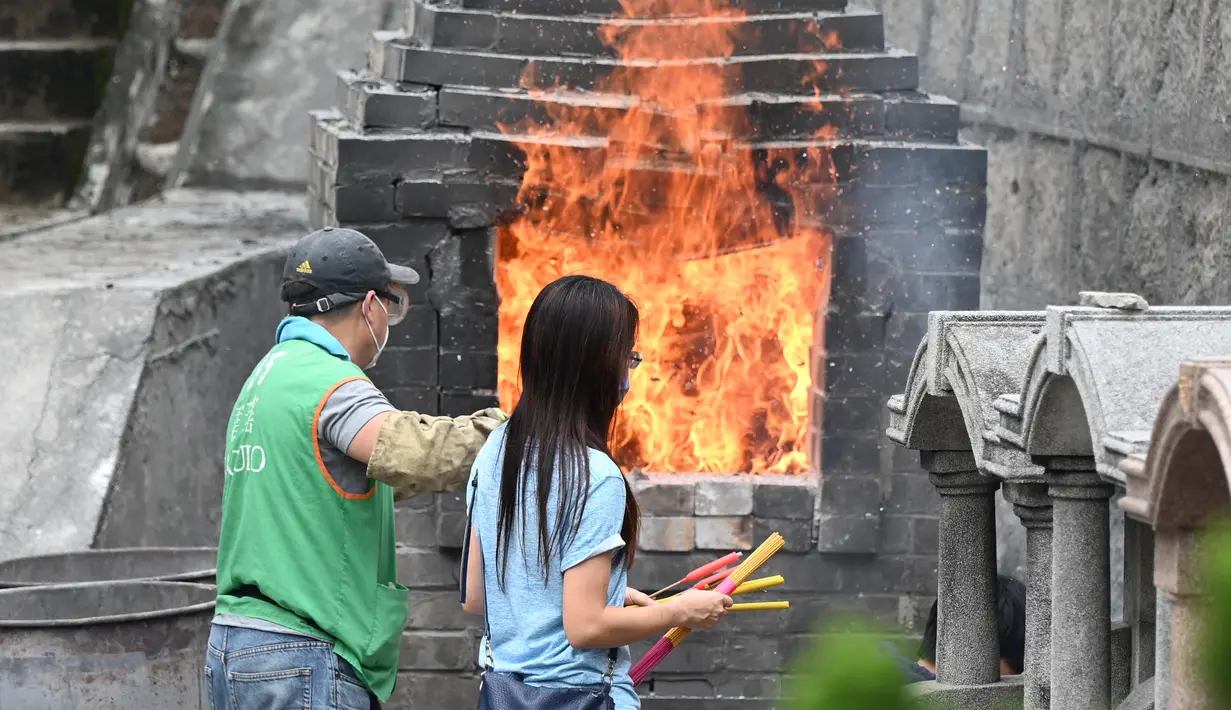 Orang-orang membakar persembahan untuk memberi penghormatan kepada orang tercinta yang telah meninggal di Pemakaman China Cape Collinson, dekat Chai Wan, Hong Kong, 5 April 2021. Kegiatan ini untuk menandai Festival Ching Ming yang juga dikenal sebagai pembersihan makam. (Peter PARKS/AFP)