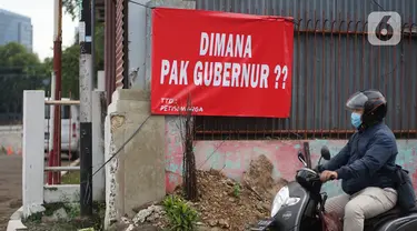 Pengguna jalan melintas di depan poster protes warga terhadap pembangunan flyover di kawasan Tanjung Barat, Jakarta, Rabu (15/7/2020). Dalam poster protes tersebut, warga menuntut agar pembayaran pelunasan pembebasan lahan segera diselesaikan secara serentak. (Liputan6.com/Immanuel Antonius)