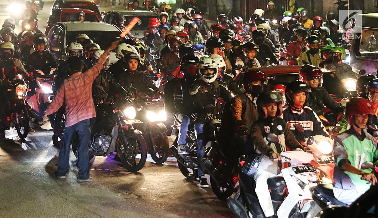 Seorang pria mengatur arus lalu lintas pemudik bersepeda motor di ruas Kalimalang, Bekasi, Kamis (22/6). Pada malam hari peningkatan kendaraan pemudik terutama yang menggunakan roda dua jauh lebih tinggi dibanding siang hari. (Liputan6.com/Angga Yuniar)