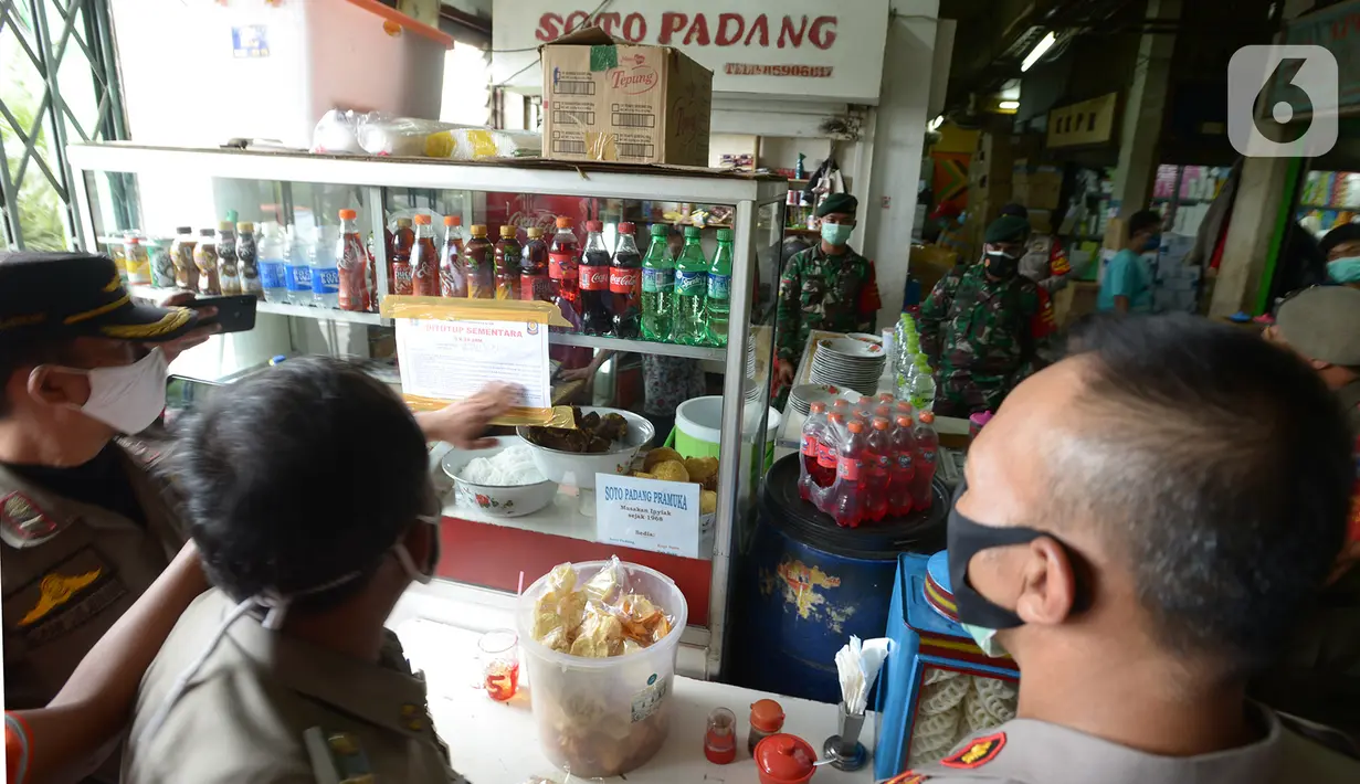 Petugas gabungan menempelkan segel penutupan sementara salah satu tempat makan di Pasar Pramuka, Jakarta, Kamis (24/9/2020). Upaya mencegah penularan virus corona terus dilakukan dengan merazia penggunaan masker dan tempat usaha makan yang masih melayani makan di tempat. (merdeka.com/Imam Buhori)