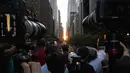 Orang-orang mengambil gambar saat matahari terbenam di Manhattan ketika fenomena "Manhattanhenge" di 42nd street, New York, Senin (11/7/2022). Fenomena Manhattanhenge hanyaterjadi di musim panas, tepatnya diantara bulan Mei hingga Juli. (Yuki IWAMURA / AFP)