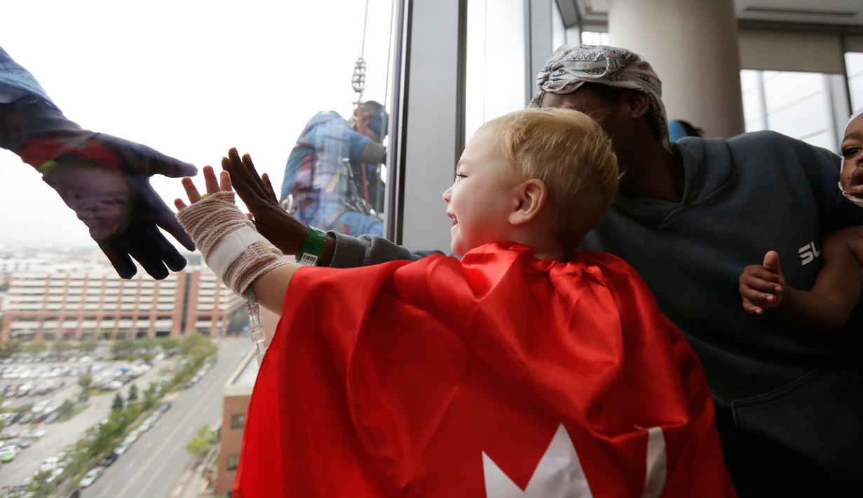 Pasien anak berusaha menyentuh tangan superhero Superman yang membersihkan kaca jendela kamar di sebuah rumah sakit di Birmingham, Rabu (11/10). Para pekerja bergelantungan di luar jendela dengan mengenakan kostum superhero. (AP Photo/Brynn Anderson)