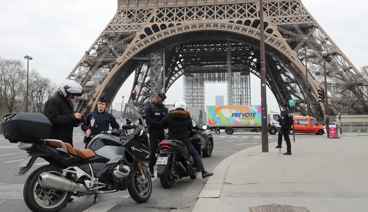 Polisi memeriksa dokumen pengemudi kendaraan saat lockdown di depan Menara Eiffel, Paris, Prancis, Rabu (18/3/2020). Pemerintah Prancis memberlakukan denda 135 Euro bagi warga keluar rumah tanpa pernyataan tertulis yang dibenarkan. (Ludovic MARIN/AFP)