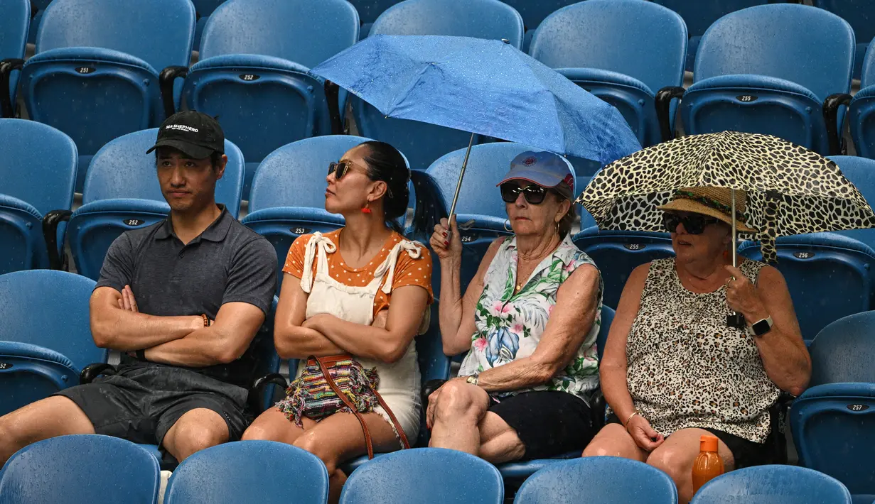 Penonton menggunakan payung untuk berlindung dari hujan saat penangguhan pertandingan perempat final tunggal putri antara petenis Kazakhstan Elena Rybakina dan petenis Latvia Jelena Ostapenko pada hari kesembilan turnamen tenis Australia Open di Melbourne pada 24 Januari 2023.
(ANTHONY WALLACE / AFP)