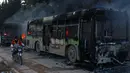Pengendara motor melewati bus yang diserang dan dibakar saat dalam perjalanan ke al-Foua dan Kefraya di dekat Idlib, Suriah, Minggu (18/12). Bus itu sedianya untuk mengevakuasi warga yang sakit dan terluka di Aleppo timur. (REUTERS/Ammar Abdullah)