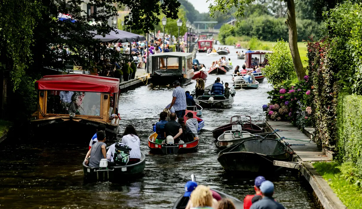 Wisatawan menaiki perahu menyusuri sungai di Giethoorn yang menjadi tujuan wisata favorit di Belanda pada 6 Agustus 2019. Mendapat julukan 'Venice of the North', kota tersebut menggunakan kanal-kanal sebagai jalan dan lalu lalang transportasi sehari-hari. (Robin van Lonkhuijsen/ANP/AFP)