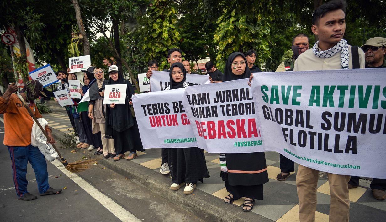 Seorang pekerja menyapu jalan saat para aktivis mengadakan unjuk rasa menentang pencegatan kapal-kapal yang berpartisipasi dalam armada Global Sumud Flotilla (GSF), sebuah misi bantuan kemanusiaan ke Gaza melalui jalur laut, di Surabaya, Jawa Timur pada Kamis 21 Mei 2026. (JUNI KRISWANTO/AFP)