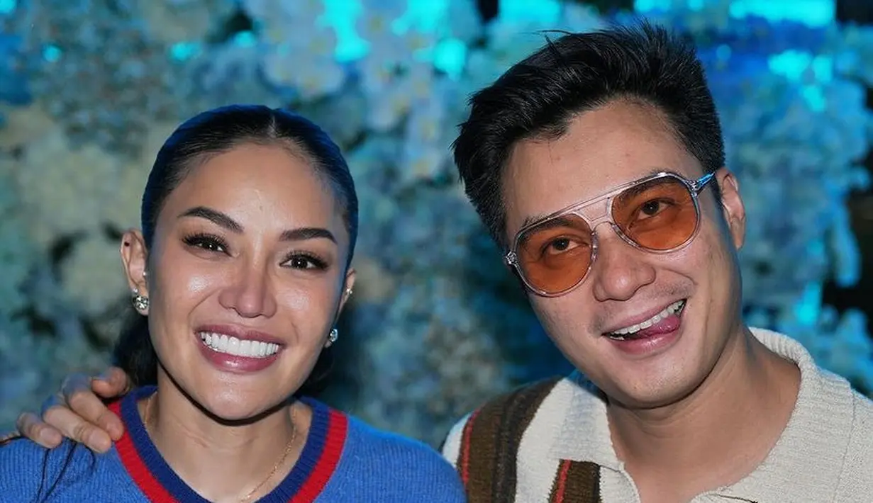 Baim wong hadie mengenakan atasan knitwear berkerah, dengan motif blaster coklat, putih, orange. Ia pun mengenakan kacamata berlensa orange, [@baimwong]