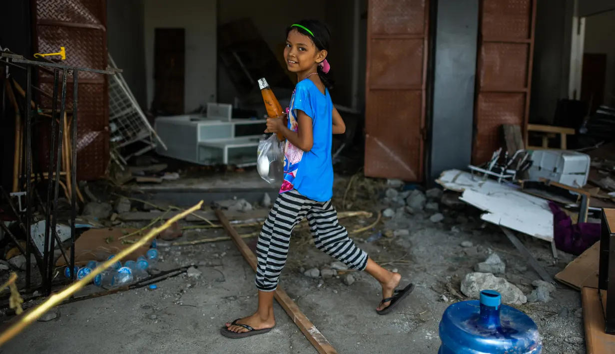 Seorang anak berjalan di antara puing-puing di sepanjang daerah pantai setelah gempa dan tsunami di Palu, Selasa (2/10). Data terbaru BNPB menunjukkan, korban tewas akibat tsunami dan gempa di Sulawesi Tengah sudah mencapai 1.347 orang. (AFP/Mohd RASFAN)