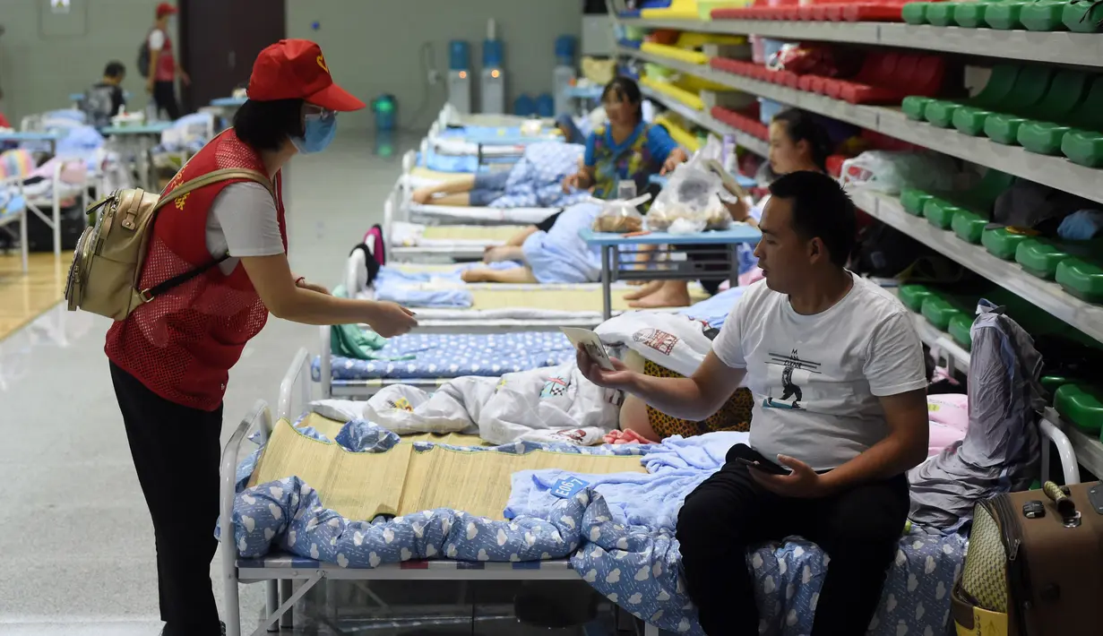 Sukarelawan memberikan buklet instruksi keselamatan kepada penduduk desa di tempat pengungsian sementara Sekolah Menengah No.168, Hefei, Provinsi Anhui, China, Rabu (29/7/2020). Lebih dari 300 penduduk desa di Kota Sanhe, Hefei, dievakuasi ke sekolah itu akibat terdampak banjir. (Xinhua/Liu Junxi)