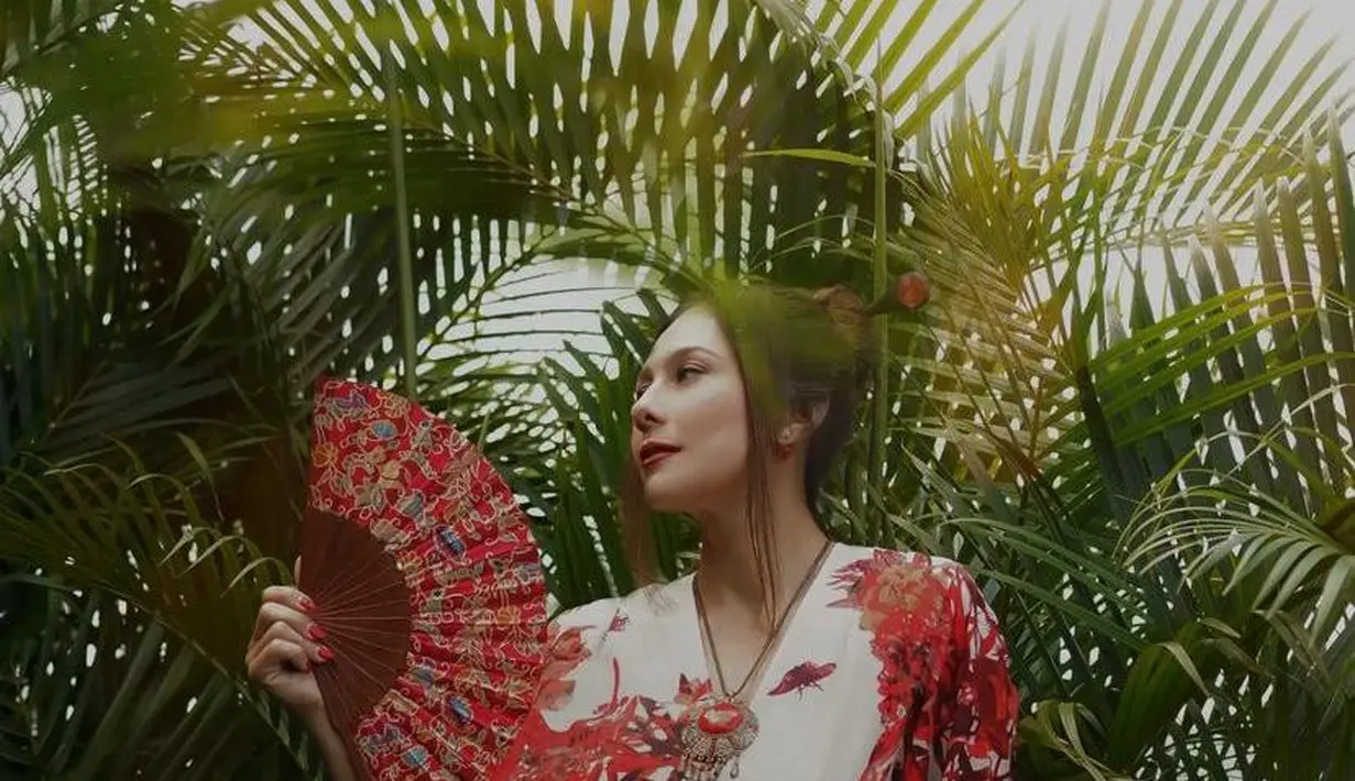 Wulan Guritno tampil mengenakan v-neck dress dominasi warna merah dari Arturro, lengkap dengan kipas lipat. [@theomono/@wulanguritno].