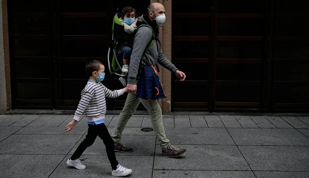 Seorang ayah dengan anak-anaknya mengenakan masker untuk mencegah virus corona berjalan-jalan di jalan pejalan kaki Carlos III, di Pamplona, Spanyol utara (27/4/2020). (AP Photo/Alvaro Barrientos)