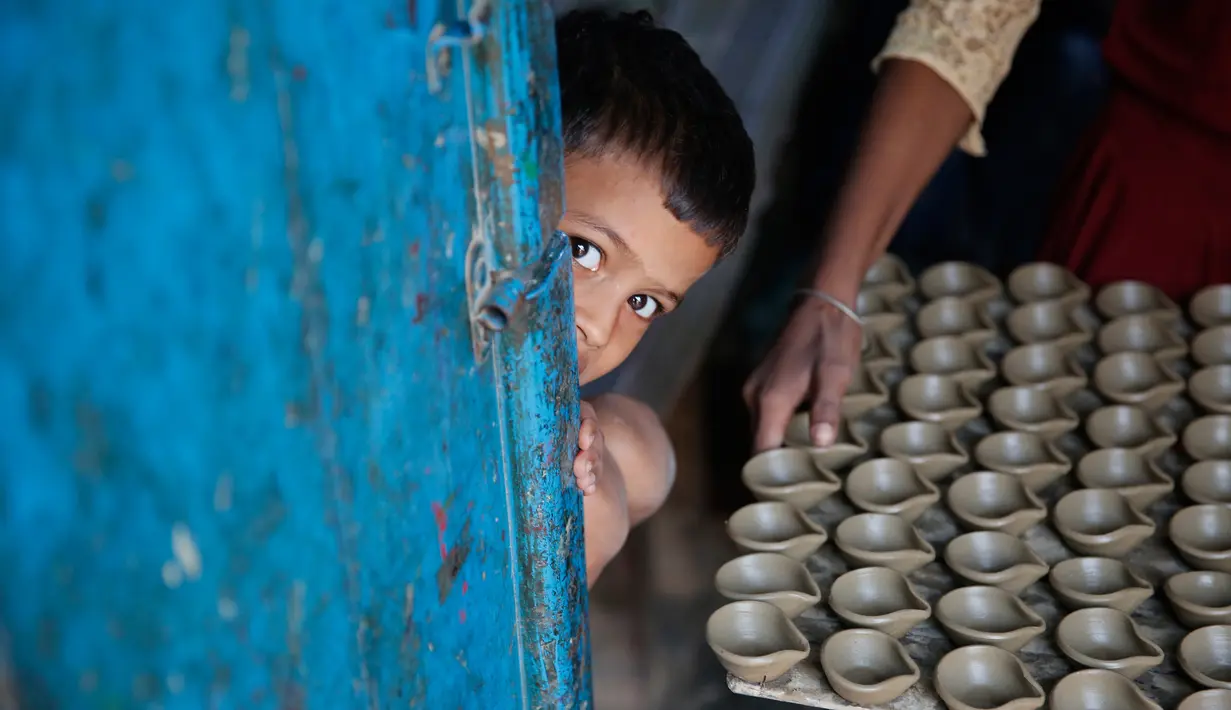 Seorang anak melihat keluar pintu ketika pengrajin tembikar membawa lampu minyak yang terbuat dari tanah liat untuk dikeringkan menjelang festival Diwali di Prayagraj, India, Kamis (17/10/2019).  Diwali merupakan festival lampu yang penting bagi umat Hindu di seluruh dunia. (AP/Rajesh Kumar Singh)