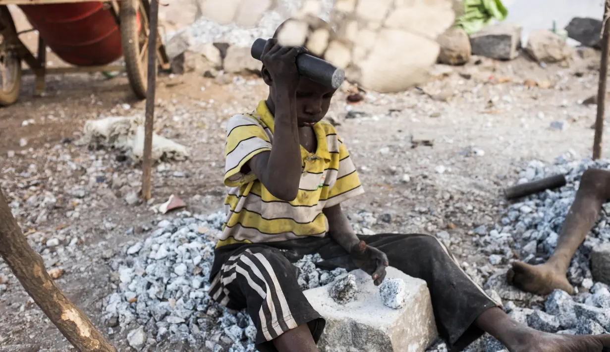 Seorang bocah tampak memecahkan batu di sebuah tambang di Ouagadougou, Burkina Faso, 21 Desember 2015. Pada 12 Juni, Organisasi perburuhan Internasional melakukan aksi menentang mempekerjakan anak dibawah umur. (NABILA EL Hadad / AFP)