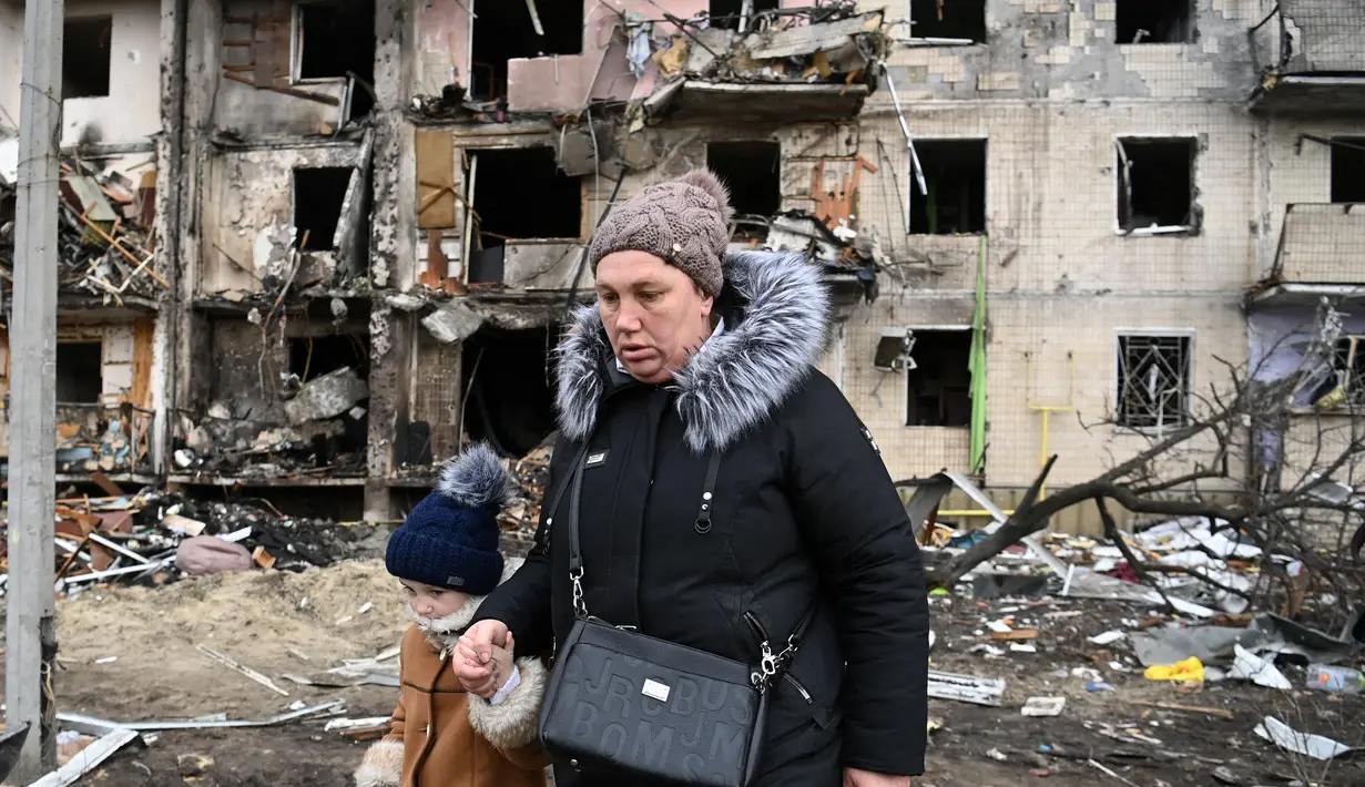 Seorang wanita berjalan di depan bangunan yang rusak setelah peluru militer Rusia menghantam di Koshytsa Street, Kiev, Ukraina (25/2/2022). Ledakan di Kiev memicu kekerasan setelah Presiden Rusia Vladimir Putin menentang peringatan Barat untuk melancarkan invasi darat skala penuh. (AFP/Daniel Leal)