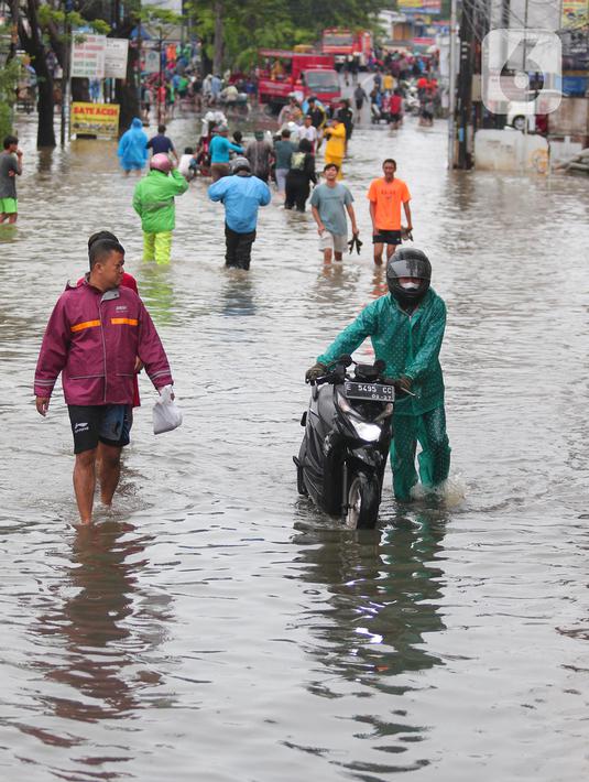 Warga berusaha melintasi genangan air ketika banjir merendam Jalan KH. Hasyim Ashari, Tangerang, Banten, Sabtu (16/7/2022). Akibat luapan kali angke ruas jalan yang menghubungkan Tangerang-Jakarta itu terputus akibat banjir. (Liputan6.com/Angga Yuniar)